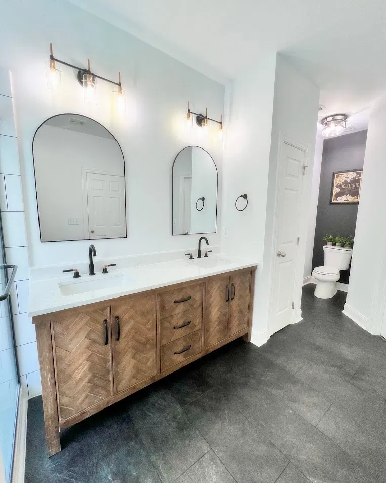 Bathroom with herringbone wood vanity, dark slate floor tile, and arch mirrors by CNB Renovations
